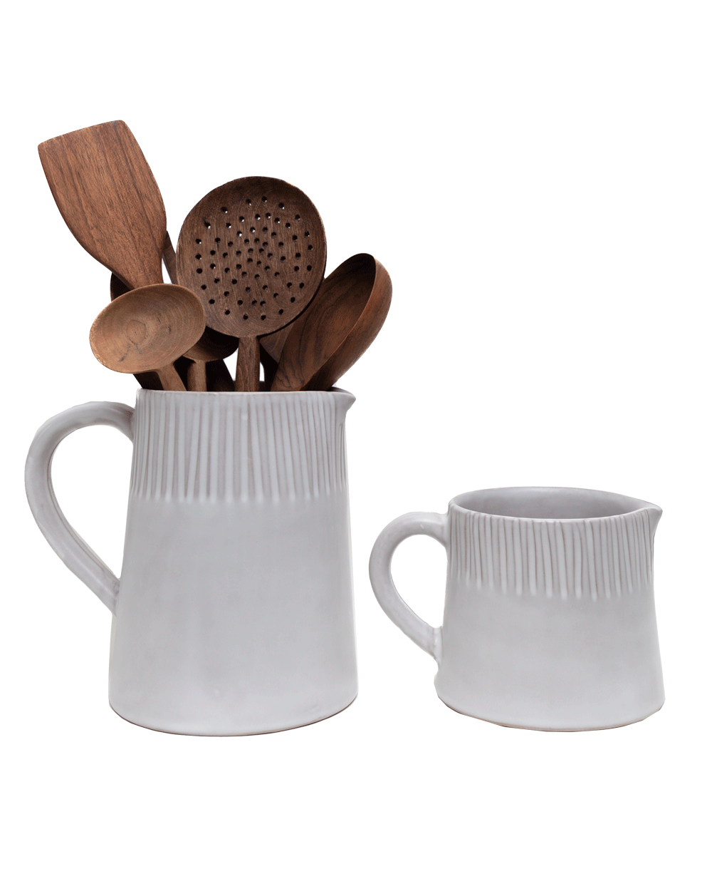 Two carved matte white pitchers, the larger one holding wooden kitchen utensils, on green