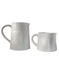 Large and small carved matte white ceramic pitchers side by side on a deep green background