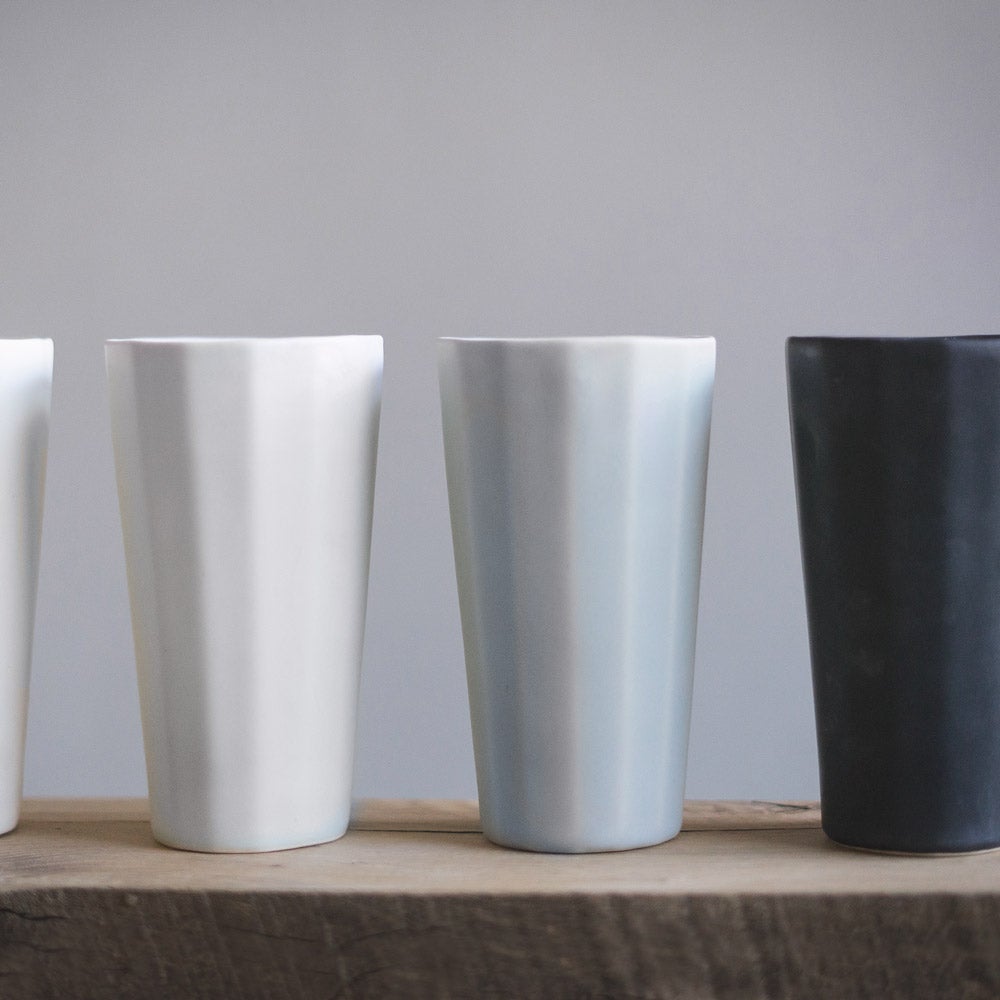 White, grey and black porcelain pint cups lined up on a wood shelf against a grey wall