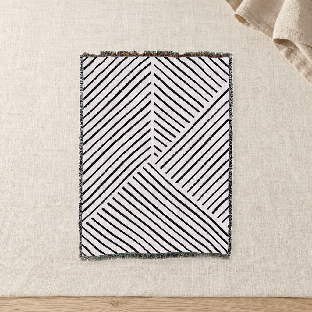 Diagonal Lines Woven Cotton Throw, Black and Ivory on raw linen with a folded napkin.