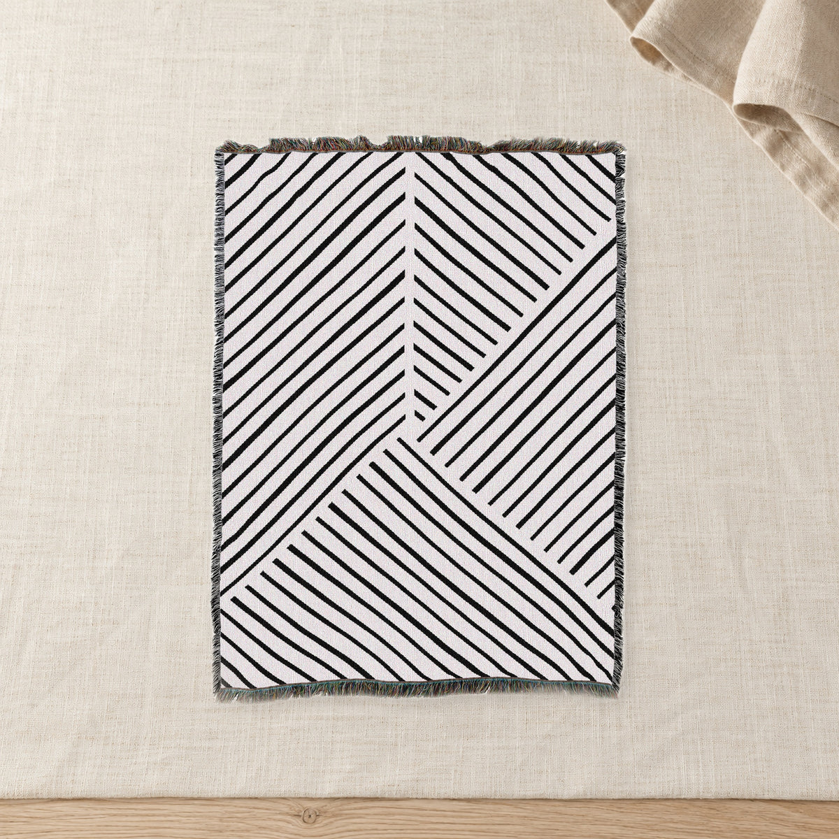 Diagonal Lines Woven Cotton Throw, Black and Ivory on raw linen with a folded napkin.