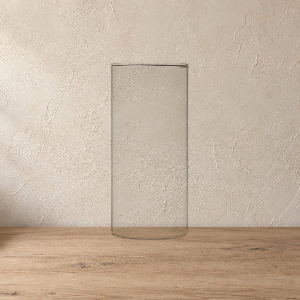 Sora Handblown Glass Cylinder Vase, 7 in on a pale wood console against a plaster wall.