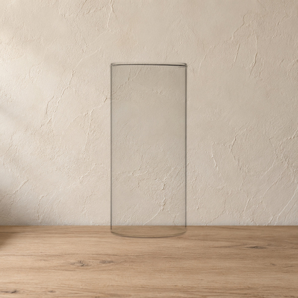 Sora Handblown Glass Cylinder Vase, 7 in on a pale wood console against a plaster wall.