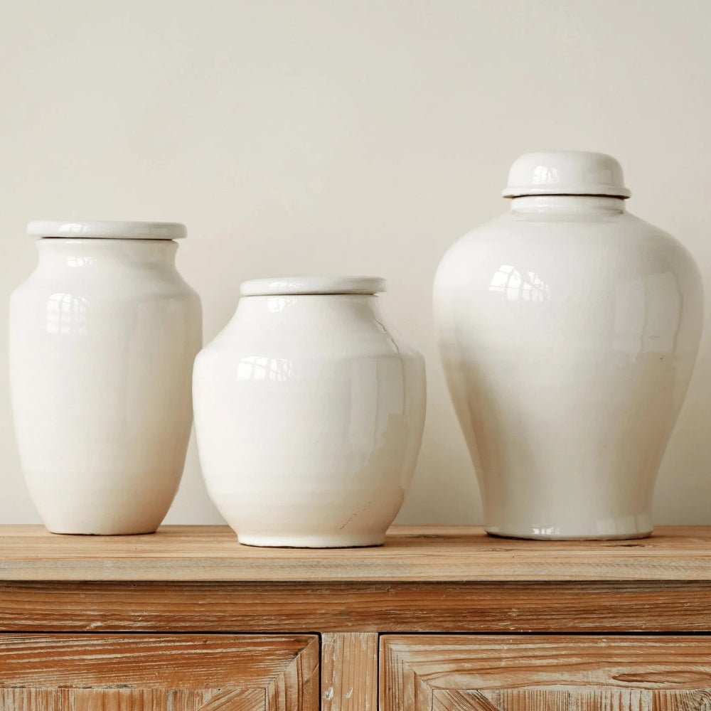 Three white glazed terracotta jars of different heights grouped on a weathered wood cabinet