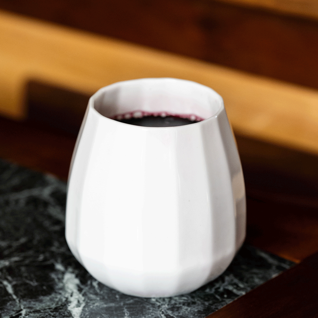 Translucent porcelain stemless wine glass of red wine on dark marble with a wood counter behind