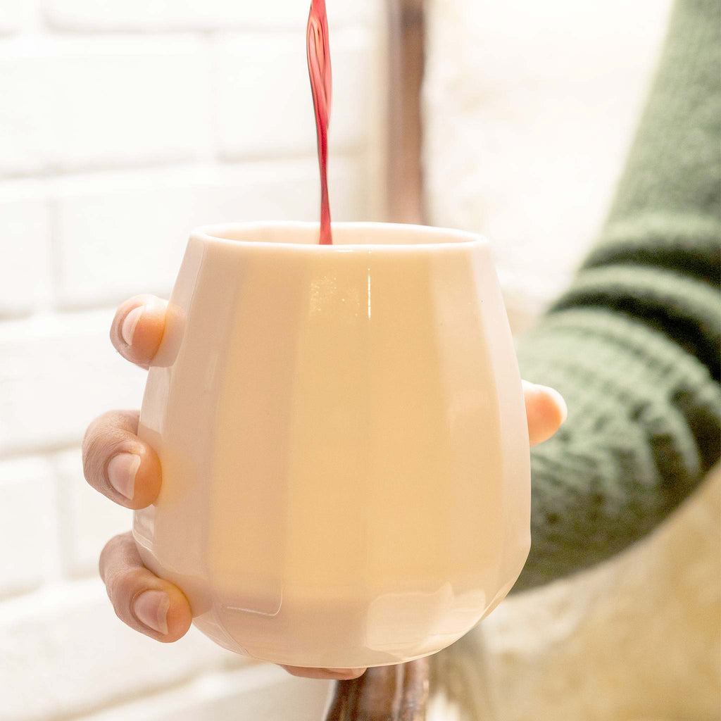 Red wine being poured into a translucent porcelain stemless wine glass held in two hands