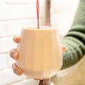 Red wine being poured into a translucent porcelain stemless wine glass held in two hands