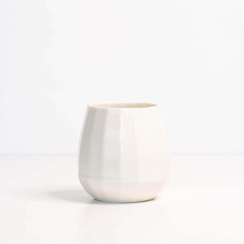 Translucent white porcelain stemless wine glass with soft facets shown alone on a white surface