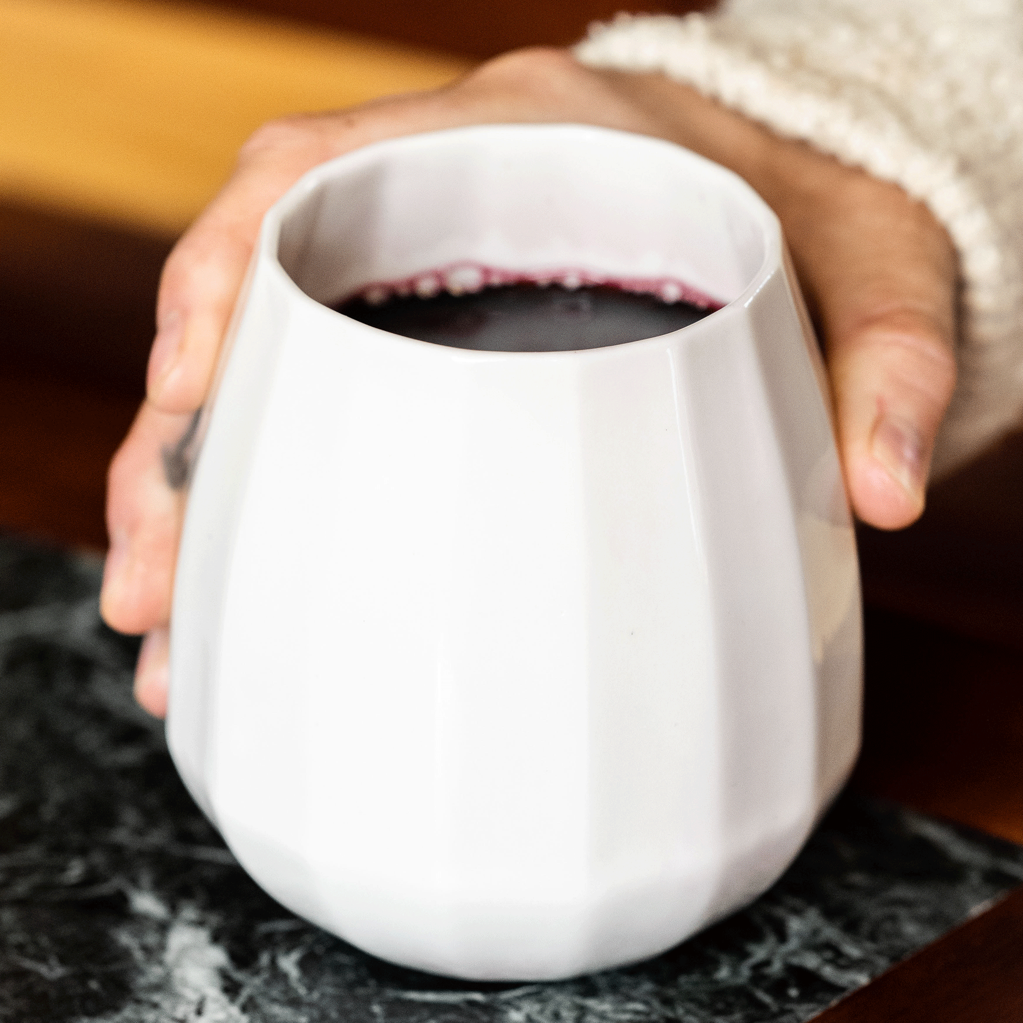 Hand holding a translucent porcelain wine glass full of red wine above a dark marble board